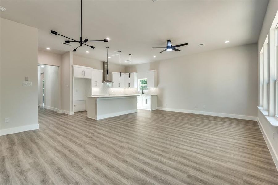 Unfurnished living room featuring ceiling fan with notable chandelier, light hardwood / wood-style floors, and sink