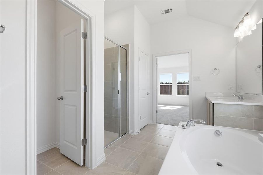 Bathroom featuring a built-in soaking tub, a glass-enclosed shower, a double vanity with a mirrored backsplash, and light-toned tile flooring