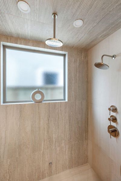 Spa-inspired steam shower wrapped in textured tile with fluted stone detailing and dual shower heads, along with a handheld wand not photographed. Spa-inspired steam shower wrapped in textured tile with fluted stone detailing and dual shower heads, along with a handheld wand not photographed.