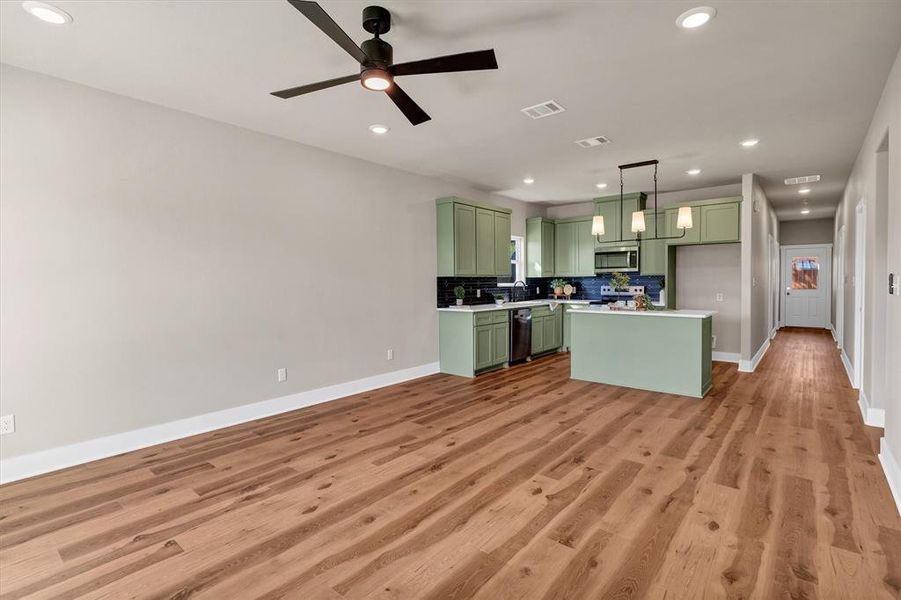Kitchen featuring green cabinetry, light countertops, backsplash, a center island, and pendant lighting Kitchen featuring green cabinetry, light countertops, backsplash, a center island, and pendant lighting