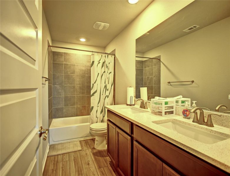 Bathroom featuring double vanity, shower / tub combo with curtain, light wood-style floors, and recessed lighting Bathroom featuring double vanity, shower / tub combo with curtain, light wood-style floors, and recessed lighting