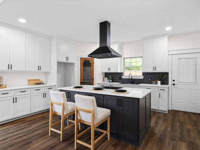 Two tone kitchen featuring two tone cabinets, a kitchen breakfast bar, ventilation hood, a center island, and dark wood finished floors