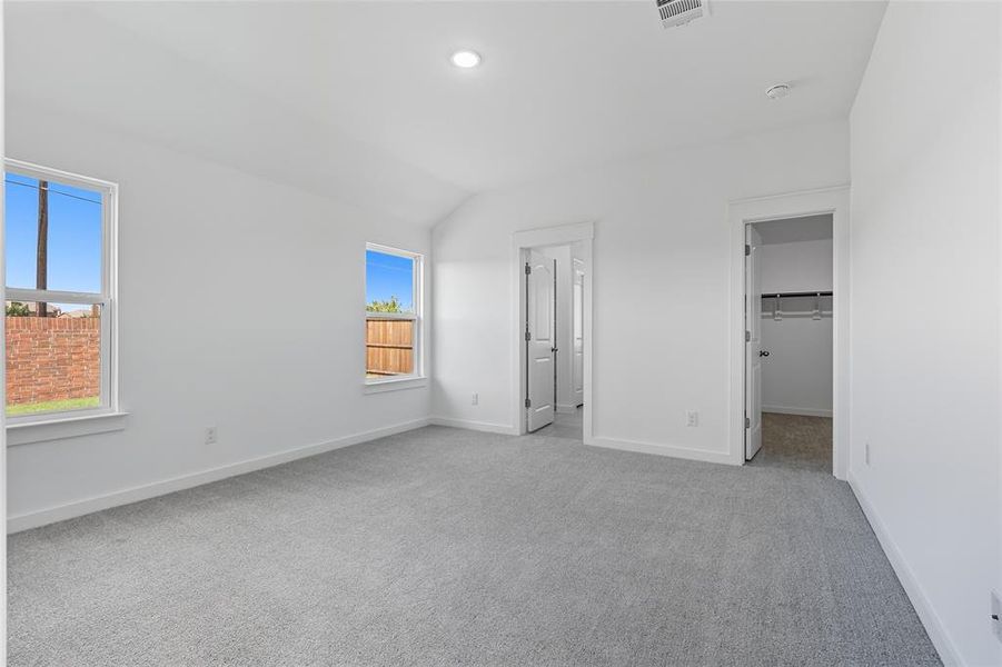 Unfurnished bedroom with a spacious closet, light carpet, vaulted ceiling, and recessed lighting Unfurnished bedroom with a spacious closet, light carpet, vaulted ceiling, and recessed lighting
