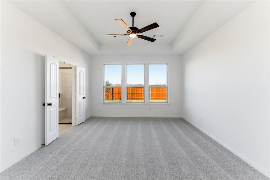 Unfurnished bedroom with carpet floors, ceiling fan, a tray ceiling, and connected bathroom