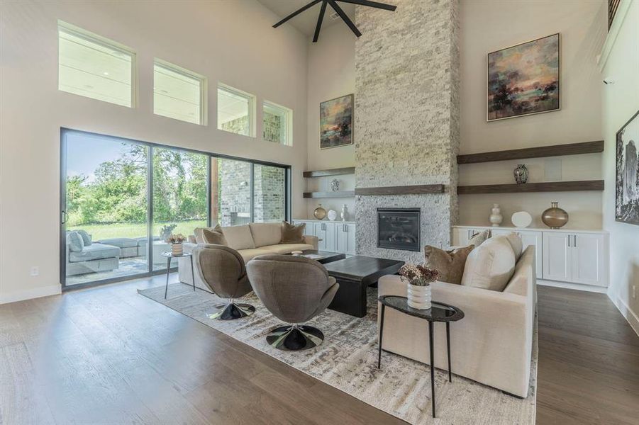 Living room with a towering ceiling, a stone fireplace, a ceiling fan, wood finished floors, and built in features Living room with a towering ceiling, a stone fireplace, a ceiling fan, wood finished floors, and built in features