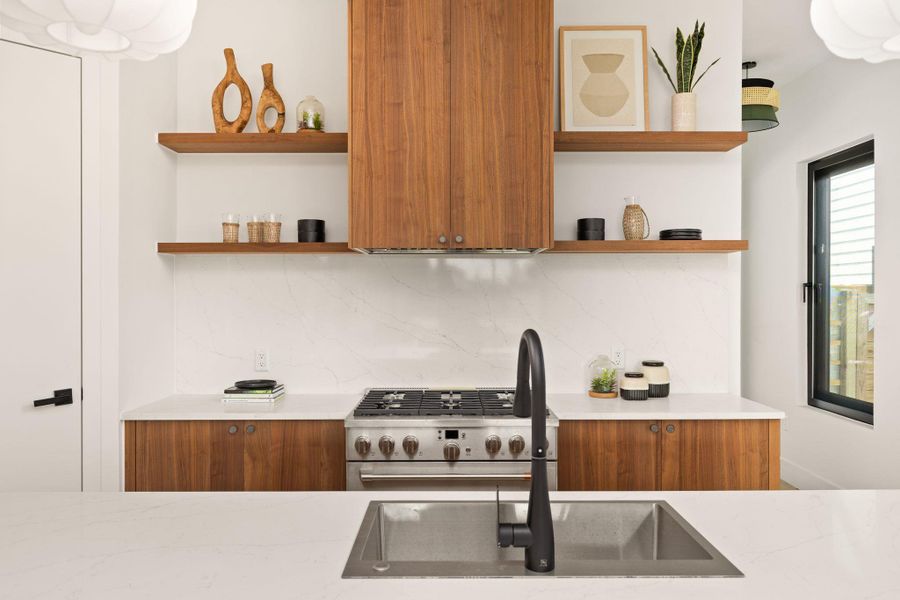 A well-appointed kitchen features rich wood cabinetry, floating shelves, and elegant quartz countertops with a modern gas range.