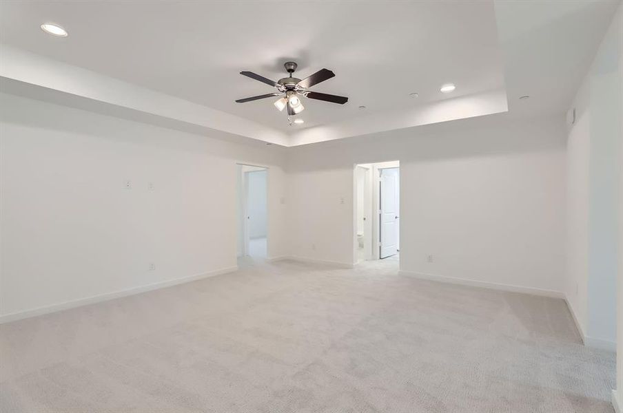 Empty room featuring ceiling fan, light carpet, and a tray ceiling