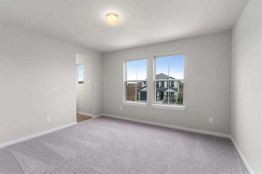 A well-lit, neutral-toned room features soft carpeting and multiple windows.