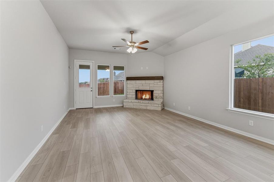 Living area featuring wood-finish flooring, a stone fireplace with a wood mantel, multiple windows, a ceiling fan, and a door to the exterior