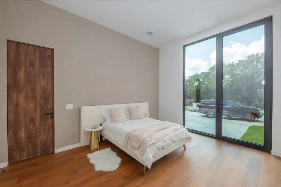 Hardwood floors and a floor-to-ceiling glass wall illuminate this bedroom.