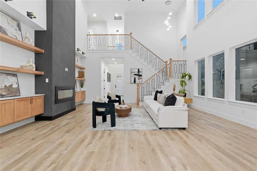 Living area with light wood-style floors, a multi sided fireplace, and a high ceiling