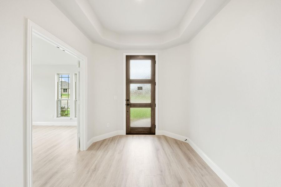 Empty room with light wood floors, tray ceiling, and wood back door with glass panels