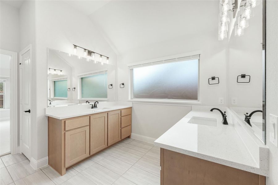 Bathroom with dual vanities, wood cabinets, white quartz countertops, and vaulted ceiling with frosted window