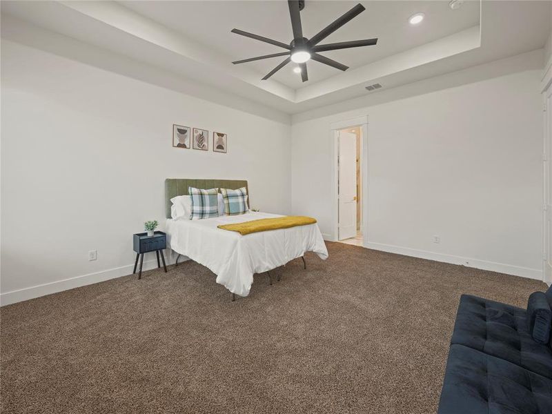 Carpeted bedroom with a ceiling fan and a raised ceiling