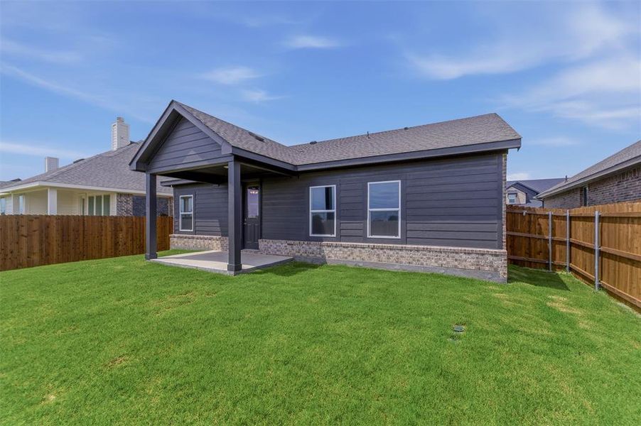 Expansive backyard featuring a covered patio, dark gray siding, brick wainscoting, and a full wood fence