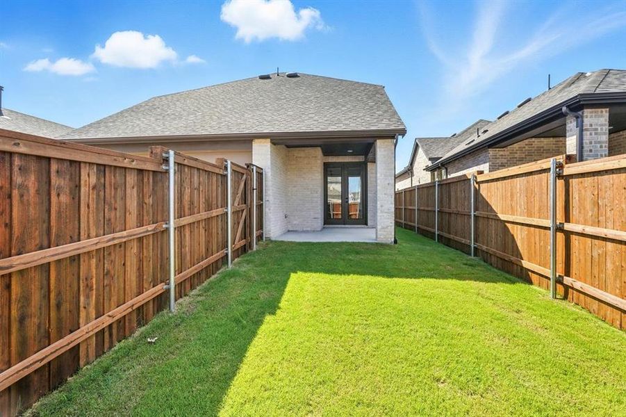 Rear view of house with a patio, brick siding, french doors, roof with shingles, and a fenced backyard Rear view of house with a patio, brick siding, french doors, roof with shingles, and a fenced backyard