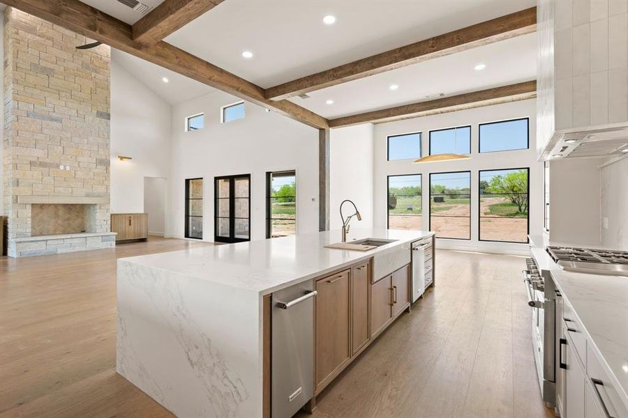 Kitchen with stainless steel appliances, a sink, light wood-style flooring, light stone counters, and beamed ceiling