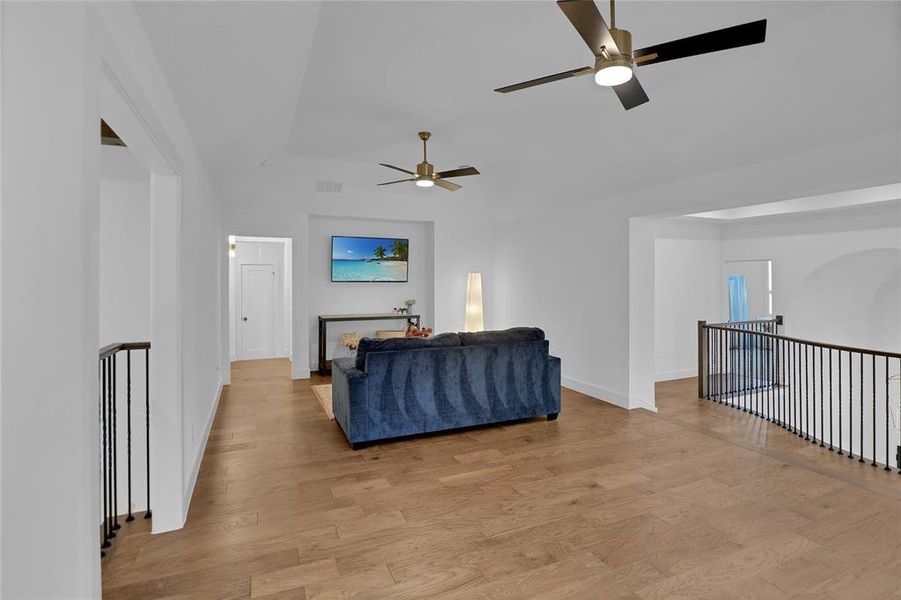 Spacious upper-level area featuring wood-finish flooring, two contemporary ceiling fans, high ceilings, and black metal railings overlooking the level below