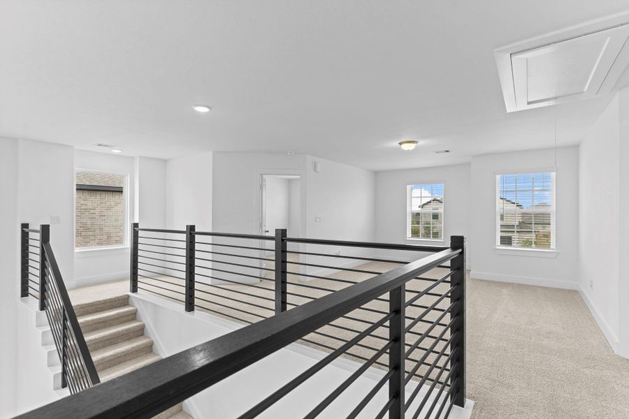 The upstairs landing offers a spacious and open feel with plush carpeting and sleek wrought iron railing, creating a stylish overlook to the lower level while connecting the secondary bedrooms and game room. **Image Representative of Plan Only and May Vary as Built**.