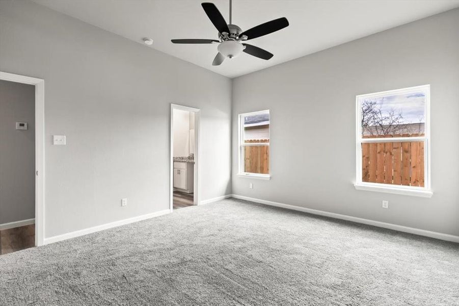 Unfurnished bedroom featuring dark colored carpet, ensuite bathroom, and ceiling fan