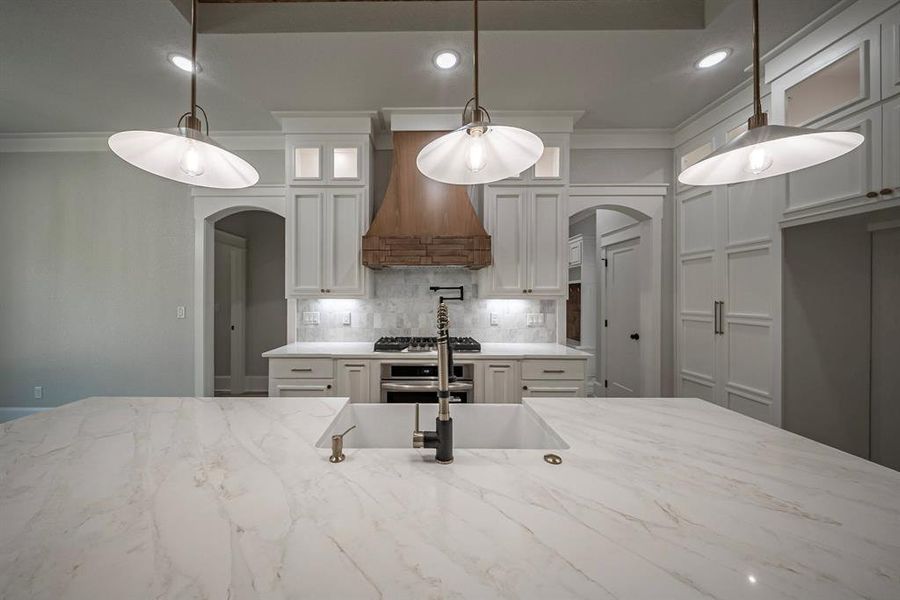 Kitchen featuring arched walkways, light stone countertops, white cabinets, crown molding, and recessed lighting Kitchen featuring arched walkways, light stone countertops, white cabinets, crown molding, and recessed lighting