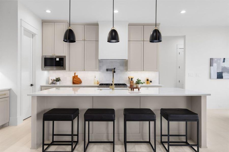 Kitchen with tasteful backsplash, a large island, stainless steel microwave, and gray cabinetry