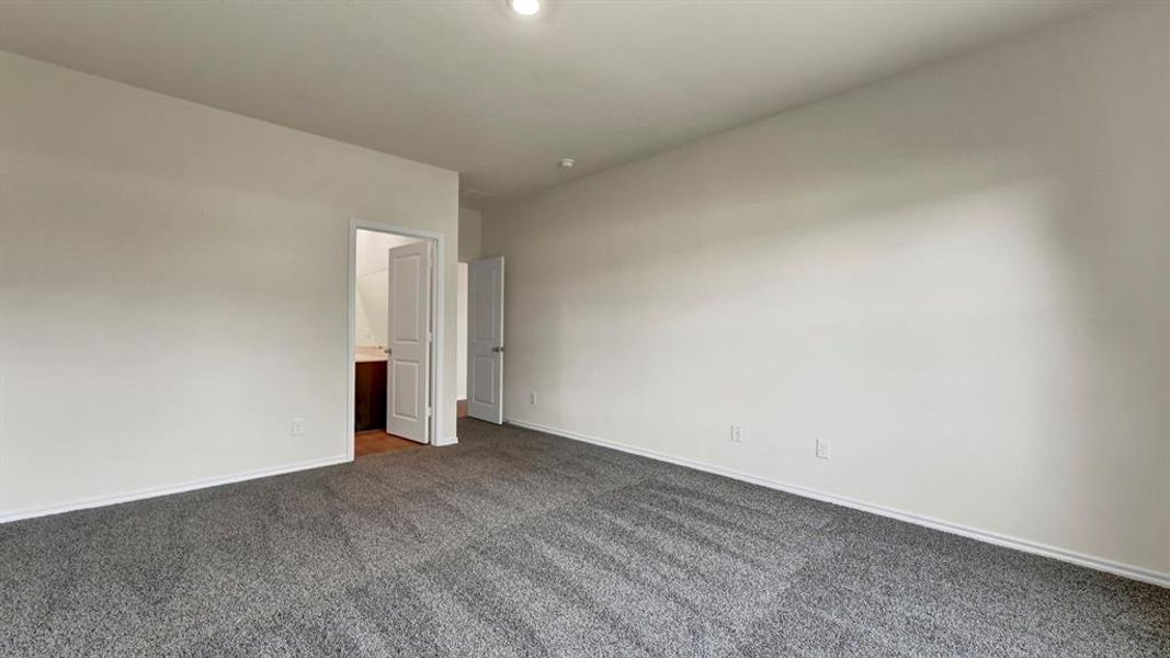 Spacious room featuring neutral tone walls, dark grey carpeting, and white baseboards