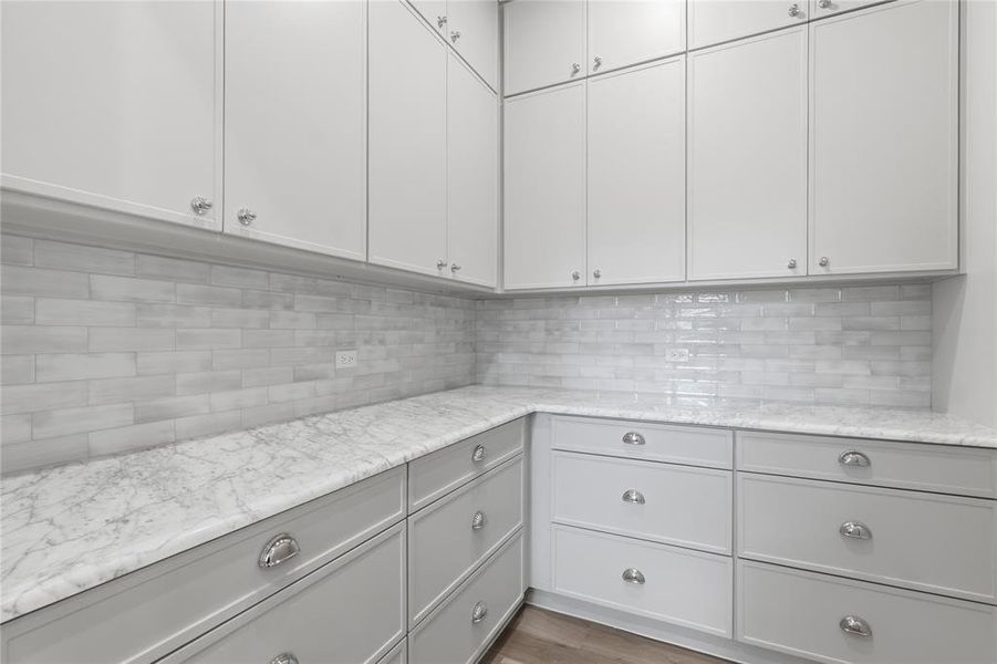 Walk-in pantry with marble countertops, custom cabinetry, and subway tile backsplash Walk-in pantry with marble countertops, custom cabinetry, and subway tile backsplash