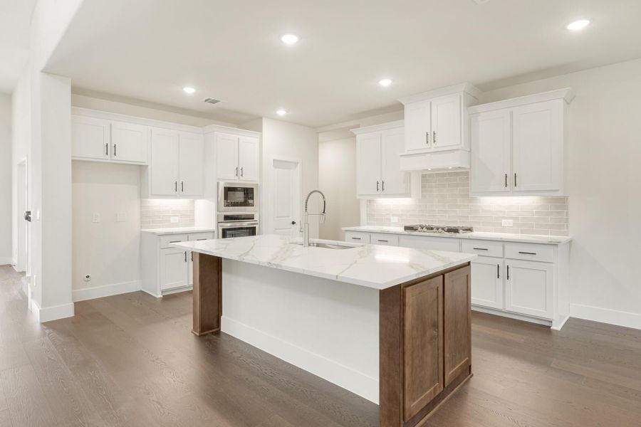 Kitchen with white cabinets, marble island, tile backsplash, and hardwood floors