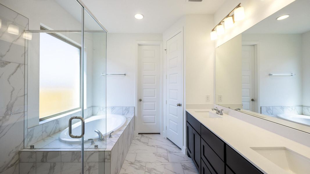 Full bath featuring double vanity, a garden tub, a marble finish shower, light marble finish flooring, and recessed lighting