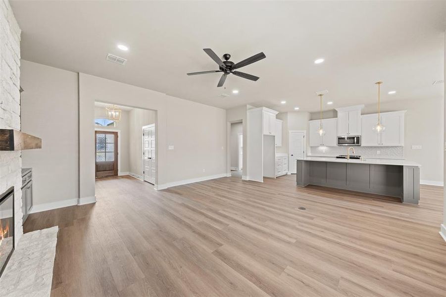 Unfurnished living room featuring ceiling fan, a stone fireplace, light wood-style floors, and recessed lighting