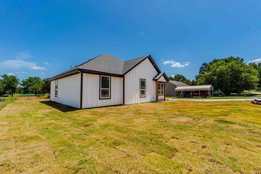 View of side of home featuring board and batten siding, a yard, roof with shingles, and a carport View of side of home featuring board and batten siding, a yard, roof with shingles, and a carport