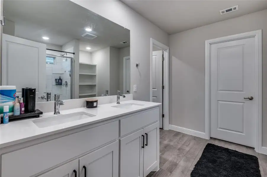 Full bath featuring a shower stall, double vanity, and light wood finished floors