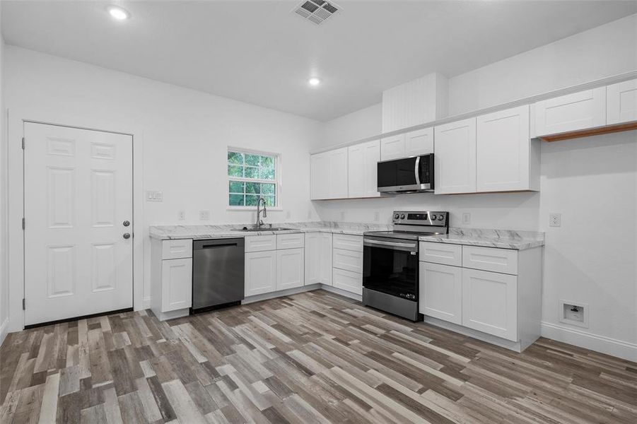 Kitchen with appliances with stainless steel finishes, white cabinets, light wood finished floors, light stone countertops, and recessed lighting
