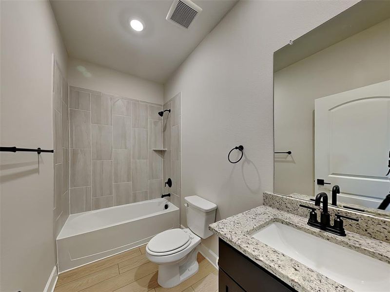 Full bathroom featuring vanity, tiled shower / bath combo, toilet, and hardwood / wood-style flooring