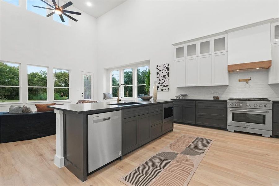 Kitchen featuring appliances with stainless steel finishes, white cabinetry, light wood finished floors, open floor plan, and a high ceiling Kitchen featuring appliances with stainless steel finishes, white cabinetry, light wood finished floors, open floor plan, and a high ceiling