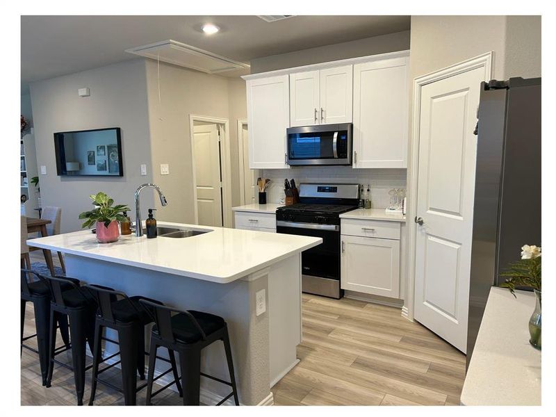 Kitchen with sink, stainless steel appliances, light hardwood / wood-style flooring, an island with sink, and white cabinets