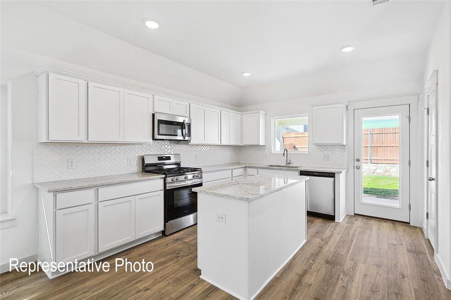 Kitchen with white cabinetry, stainless steel appliances, a center island, light stone counters, and decorative backsplash