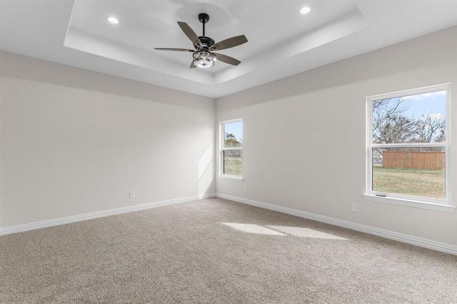 Carpeted empty room featuring ceiling fan and a tray ceiling Carpeted empty room featuring ceiling fan and a tray ceiling