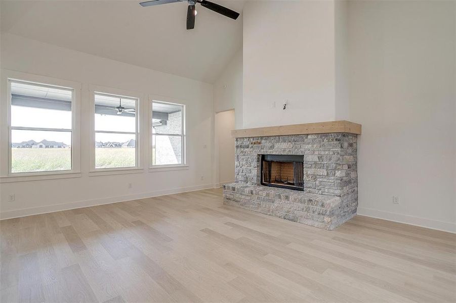 Unfurnished living room with light hardwood / wood-style flooring, high vaulted ceiling, a fireplace, and ceiling fan