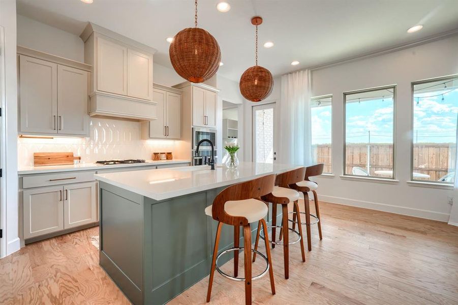 Kitchen featuring hanging light fixtures, backsplash, an island with sink, light wood-type flooring, and sink