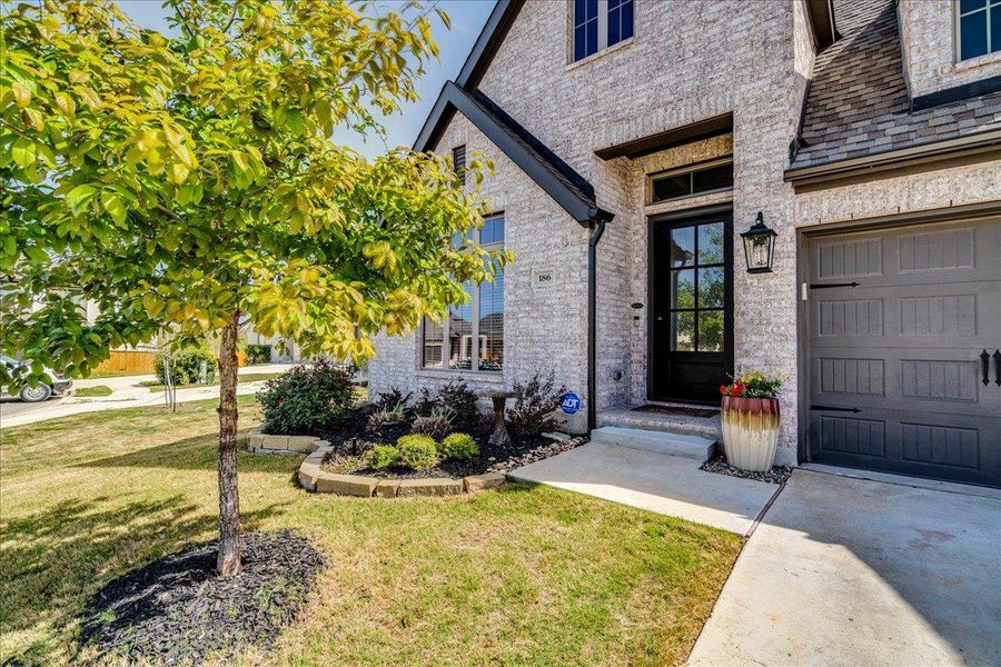 Doorway to property featuring brick siding, a lawn, and a high end roof