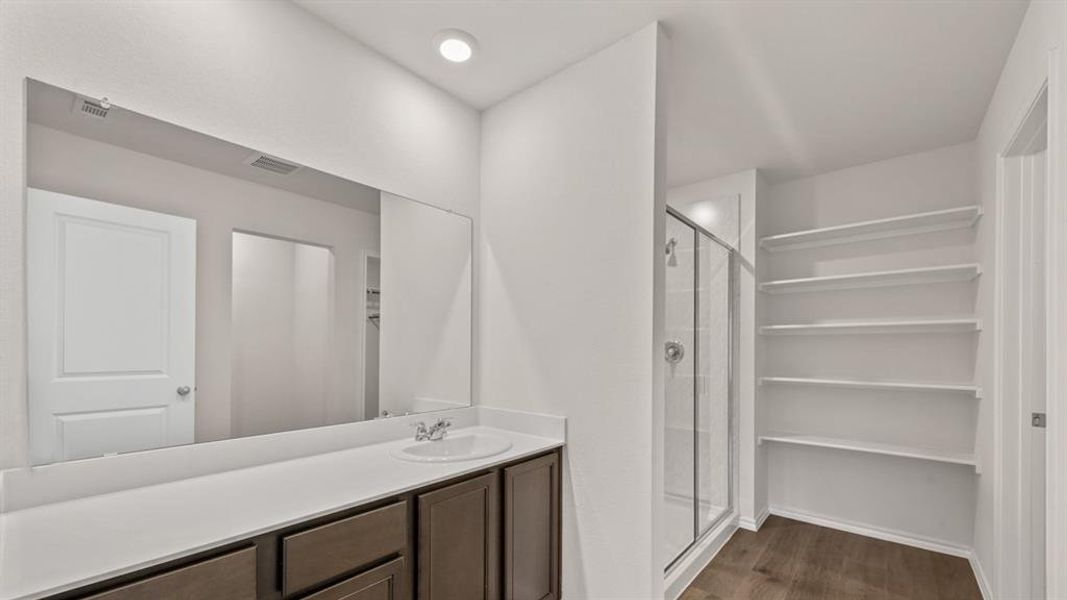 Bathroom featuring a single-sink vanity with white countertop, dark wood-finish cabinetry, a large wall-mounted mirror, and a glass-enclosed shower