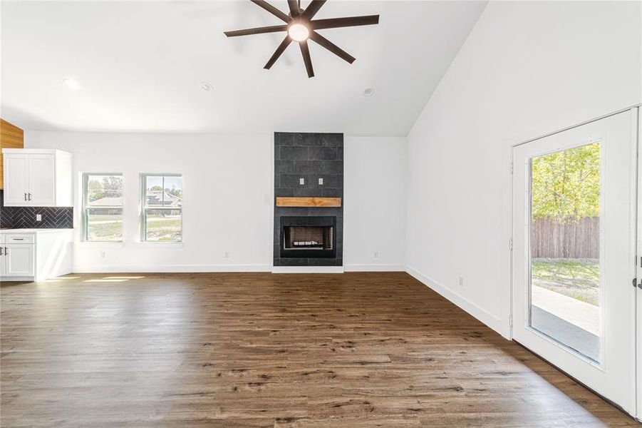 Unfurnished living room featuring dark wood-style flooring, high vaulted ceiling, a fireplace, and ceiling fan