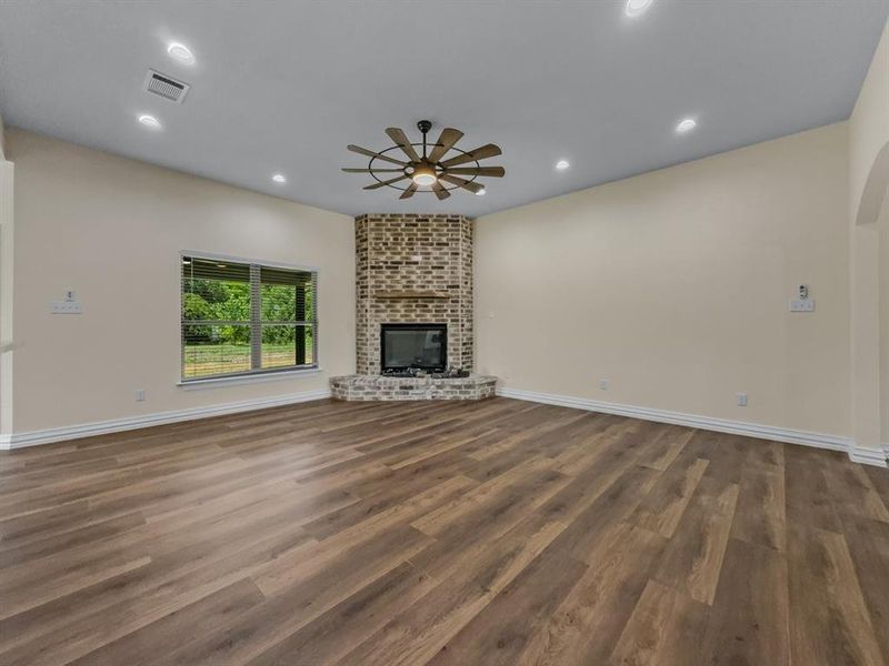 Unfurnished living room with a ceiling fan, dark wood-style floors, recessed lighting, and a brick fireplace Unfurnished living room with a ceiling fan, dark wood-style floors, recessed lighting, and a brick fireplace