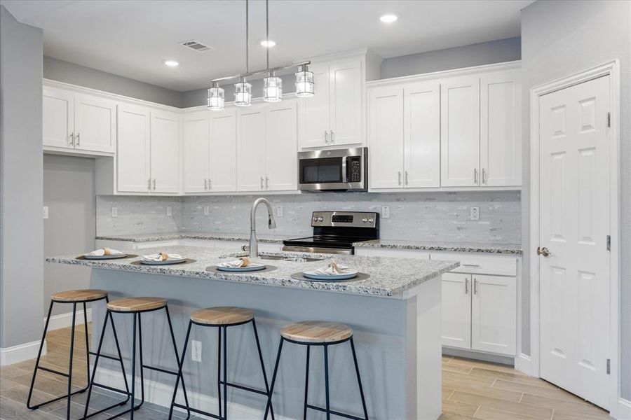 Kitchen with white cabinets, light stone countertops, a center island with sink, and appliances with stainless steel finishes