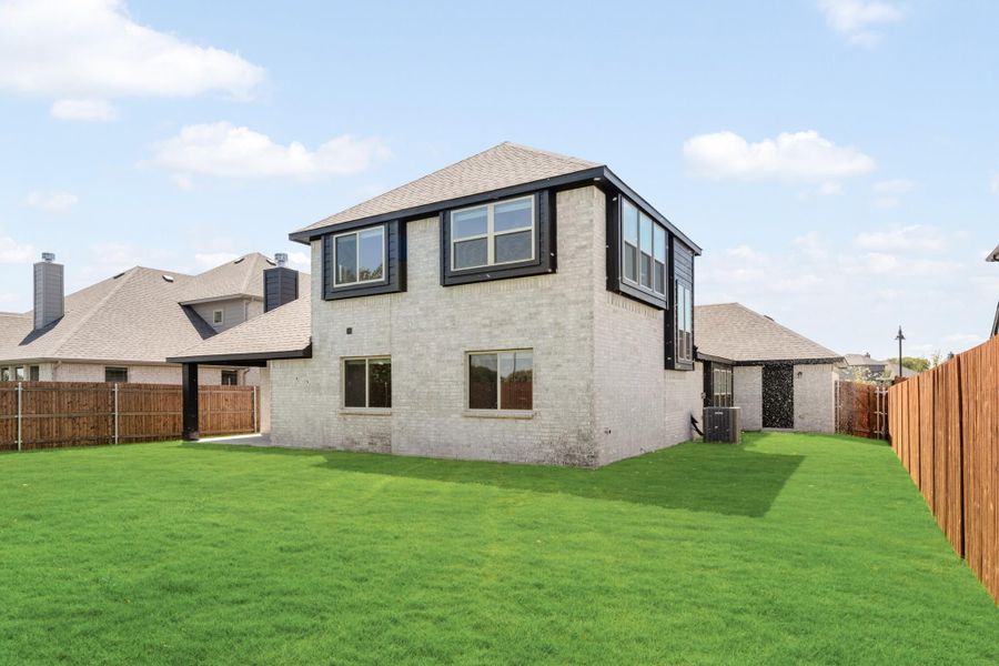 Two-story brick home rear exterior with large green backyard and wood privacy fence