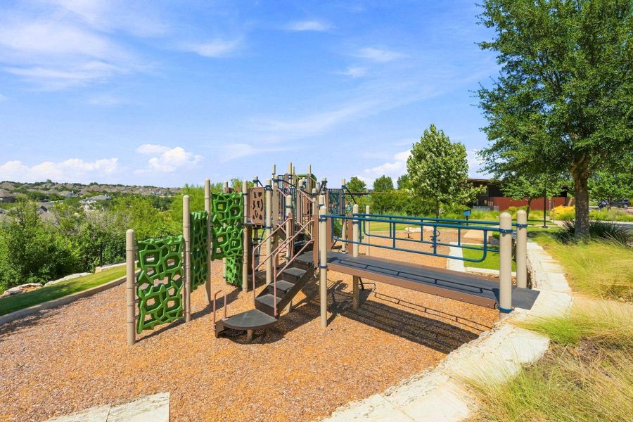 A modern community playground sits surrounded by green landscaping under a bright blue sky.