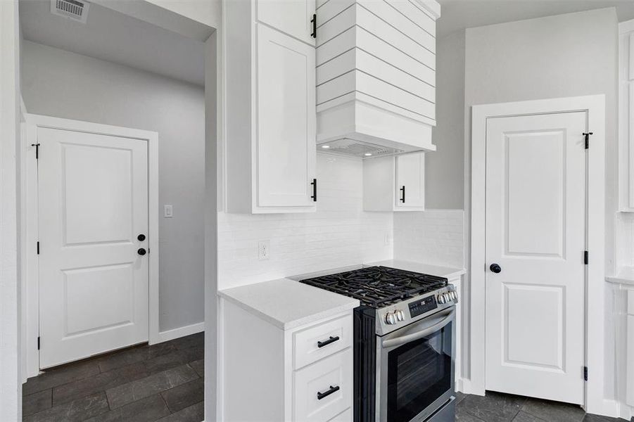 Kitchen with gas range, custom exhaust hood, light countertops, white cabinetry, and backsplash