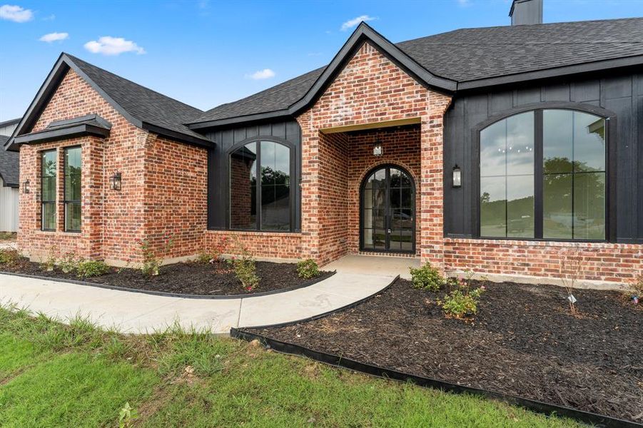 View of front of property featuring brick siding, roof with shingles, and a chimney
